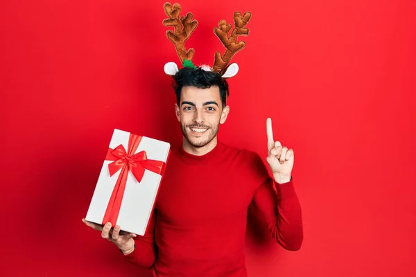 Young Hispanic Man Wearing Cute Christmas Reindeer Horns Holding Gifts — Stock Photo, Image