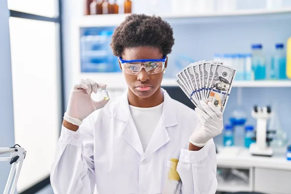 African american woman working at scientist laboratory holding dollars depressed and worry for distress, crying angry and afraid. sad expression.