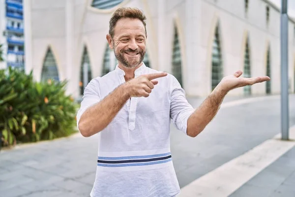 Middle age man outdoor at the city amazed and smiling to the camera while presenting with hand and pointing with finger.