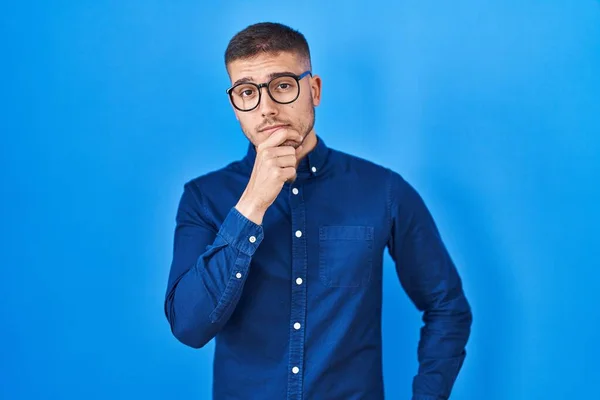 Joven Hombre Hispano Con Gafas Sobre Fondo Azul Mirando Confiado —  Fotos de Stock