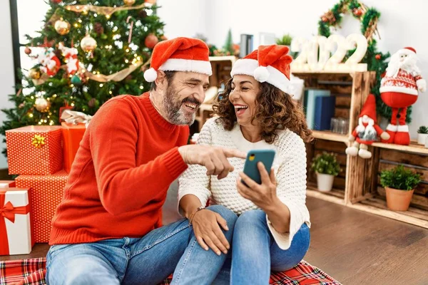 Középkorú Spanyol Házaspár Boldogan Mosolyog Karácsonyi Kalapban Ülve Padlón Okostelefonnal — Stock Fotó