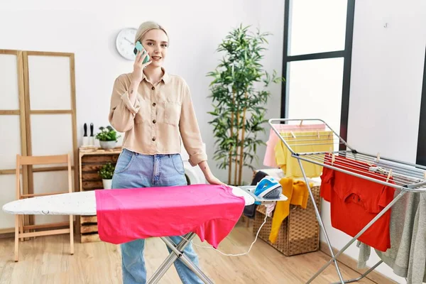 Young Caucasian Woman Talking Smartphone Ironing Clothes Laundry Room — Stockfoto