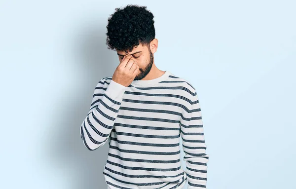 ひげを生やした若いアラブ人男性は カジュアルな縞模様のセーターを着て疲れ鼻と目をこすり疲労と頭痛を感じている ストレスとフラストレーションの概念 — ストック写真