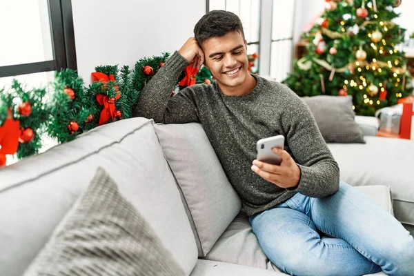 Young Hispanic Man Using Smartphone Sitting Sofa Christmas Tree Home — 图库照片