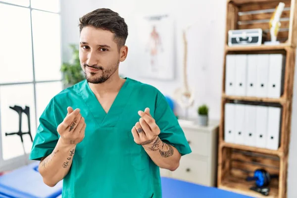 Young Physiotherapist Man Working Pain Recovery Clinic Doing Money Gesture — Stockfoto