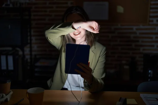 Blonde caucasian woman working at the office at night smiling cheerful playing peek a boo with hands showing face. surprised and exited