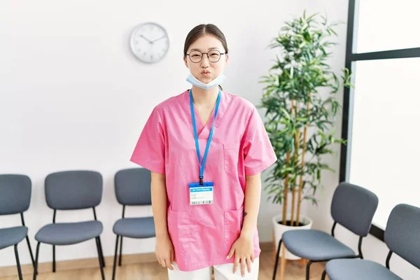 若いアジア人看護師の女性が面白い顔で頬をパフ医療待合室で 口は空気で膨らみ狂気の表情で — ストック写真