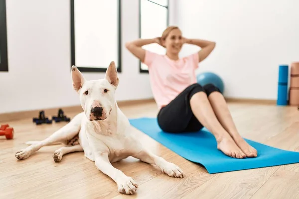 Young caucasian woman smiling confident training abs exercise with dog at sport center