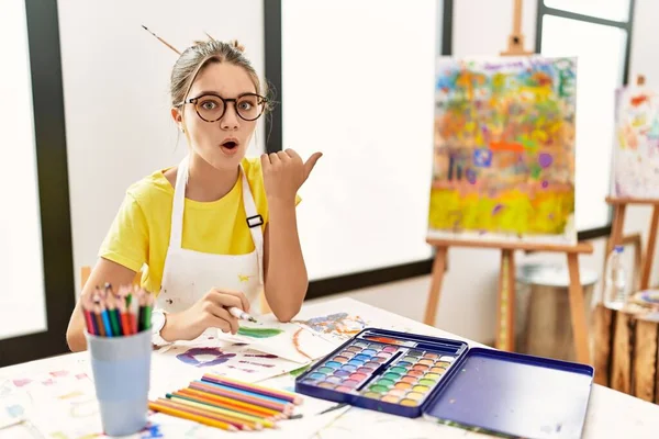 Young Brunette Teenager Art Studio Surprised Pointing Hand Finger Side — Foto Stock