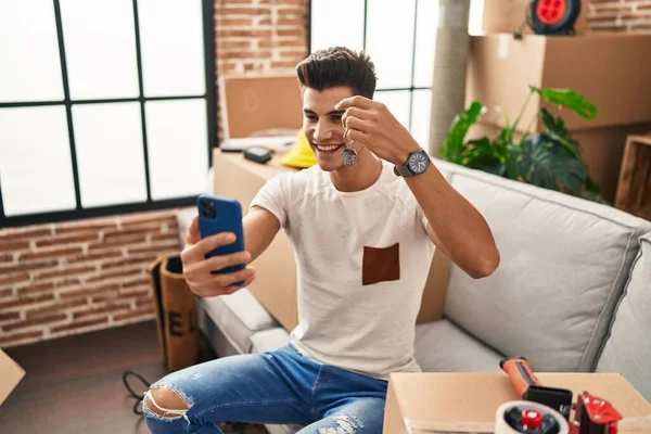 Young hispanic man having video call holding key of house at new home