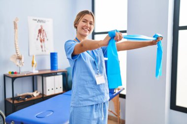 Genç İspanyol kadın fizyoterapist rehabilitasyon kliniğinde elastik bant kullanıyor.