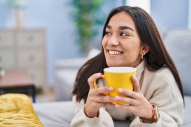 Genç İspanyol kadın evdeki kanepede kahve içiyor.