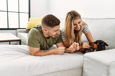 Genç İspanyol çift evde köpekle kanepede mutlu bir şekilde yatıyor..