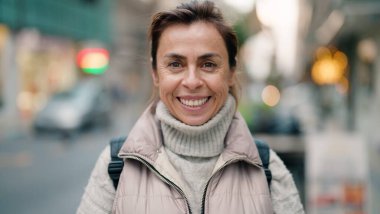 Orta yaşlı İspanyol kadın sokakta kendine güvenerek gülümsüyor.