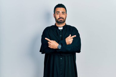 Sakallı, Katolik rahip cüppeli yakışıklı bir adam iki tarafı da parmaklarıyla işaret ediyor. Farklı yönler farklı. 