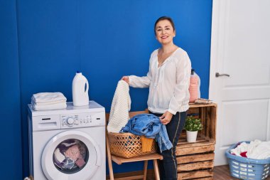 Middle age woman holding sweater washing clothes at laundry room