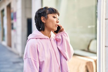 Gülümseyen genç bir kadın caddedeki akıllı telefondan konuşuyor.