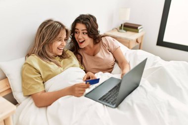 Yatak odasında kredi kartı ve laptop kullanan genç bir çift.