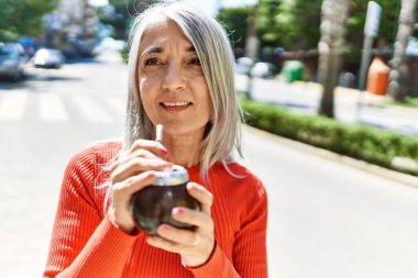 Orta yaşlı, kır saçlı, gülümseyen, mutlu, içki arkadaşı bir kadın..