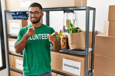 Young indian man volunteer holding donations box pointing fingers to camera with happy and funny face. good energy and vibes. 