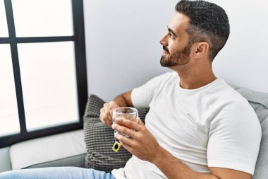 Young hispanic man smiling confident drinking tea at home
