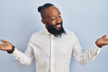 Mavi arka planda duran Afrikalı Amerikalı adam gülümsüyor. İki elini de açık tutuyor. Karşılaştırma ve reklam karşılaştırması yapıyor ve dengeyi sağlıyor. 