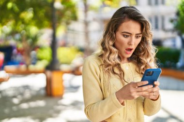 Parkta akıllı telefon kullanan genç bir kadın.