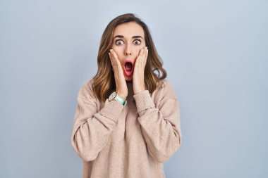 Young woman standing over isolated background afraid and shocked, surprise and amazed expression with hands on face 