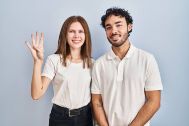 Young couple wearing casual clothes standing together showing and pointing up with fingers number four while smiling confident and happy. 
