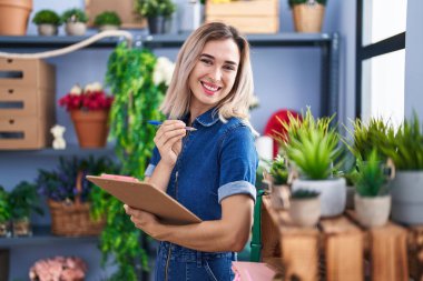 Young woman florist smiling confident holding clipboard at florist