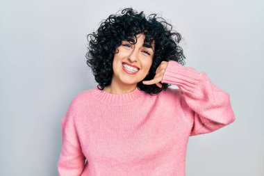Orta Doğulu genç bir kadın günlük giysiler içinde gülümsüyor telefonla el ve parmaklarıyla jest yapıyor telefonda konuşuyor gibi. iletişim kavramları. 