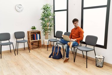 Young hispanic man smiling confident using laptop at waiting room