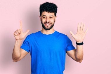 Sakallı, günlük mavi tişörtlü genç bir Arap. Yedi numaralı parmaklarıyla onu gösteriyor ve gülümsüyor. Kendinden emin ve mutlu.. 