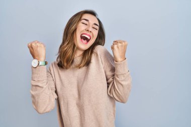 Young woman standing over isolated background celebrating surprised and amazed for success with arms raised and eyes closed. winner concept. 