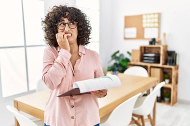 Young middle eastern woman wearing business style at office looking stressed and nervous with hands on mouth biting nails. anxiety problem. 