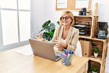 Middle age blonde woman smiling confident having video call at office