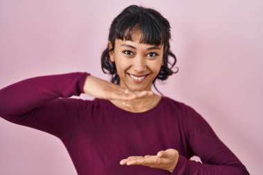 Pembe arka planda duran genç ve güzel bir kadın. Elleriyle büyük ve büyük bir işaret gösteriyor. Ölçü sembolü. Kameraya bakıp gülümsüyor. ölçüm kavramı. 