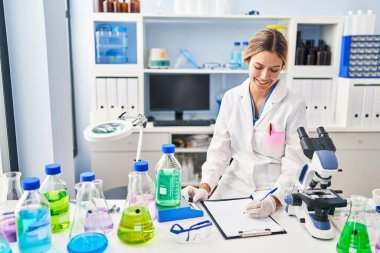 Genç İspanyol kadın bilim adamı. Sıvıyı ölçüyor. Laboratuvarda belgeye yazıyor.