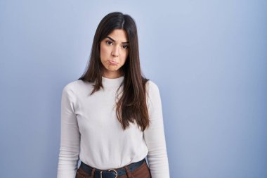 Mavi arka planda duran genç esmer kadın üzgün ve endişeli, sinirli ve korkmuş bir şekilde ağlıyor. hüzünlü ifade. 