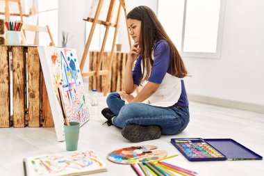 Resim stüdyosunda resim çizen şüpheyle bakan genç Latin kadın.