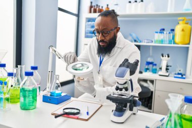 Genç Afrikalı Amerikalı adam bilim adamı üniforması giyiyor. Laboratuvarda Loupe 'u kullanıyor.