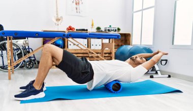 Genç İspanyol hasta klinikte köpük silindir kullanarak rehabilitasyon seansı yapıyor.