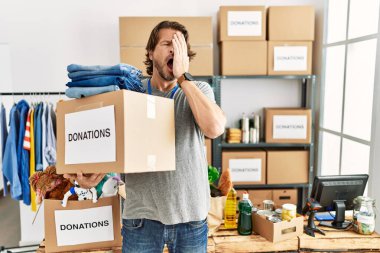 Handsome middle age man holding donations box for charity at volunteer stand yawning tired covering half face, eye and mouth with hand. face hurts in pain. 