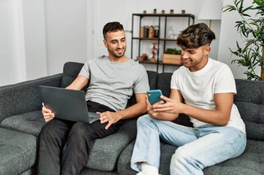 Evde akıllı telefon ve dizüstü bilgisayar kullanan iki İspanyol erkek.