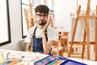 Hispanic man with beard at art studio thinking looking tired and bored with depression problems with crossed arms. 