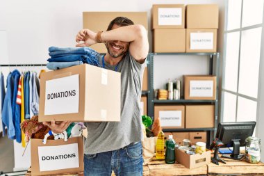 Handsome middle age man holding donations box for charity at volunteer stand smiling cheerful playing peek a boo with hands showing face. surprised and exited 