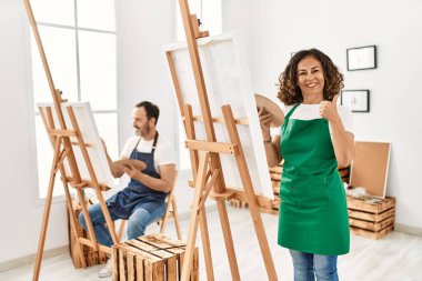 İspanyol orta yaşlı kadın ve sanat stüdyosundaki olgun adam mutlu ve olumlu gülümsüyor, başparmağıyla mükemmel ve onay işareti yapıyor. 