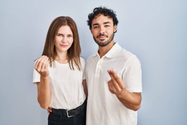 Young couple wearing casual clothes standing together doing money gesture with hands, asking for salary payment, millionaire business 