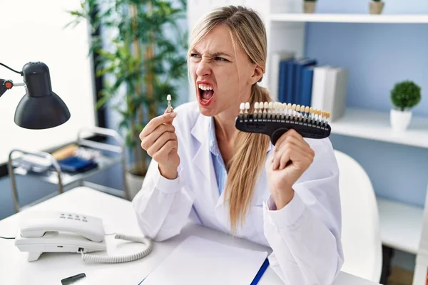 Beautiful dentist woman comparing teeth whitening angry and mad screaming frustrated and furious, shouting with anger. rage and aggressive concept. 