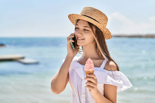 海辺でアイスクリームを食べるスマートフォンで話す愛らしい女の子の観光客 — ストック写真